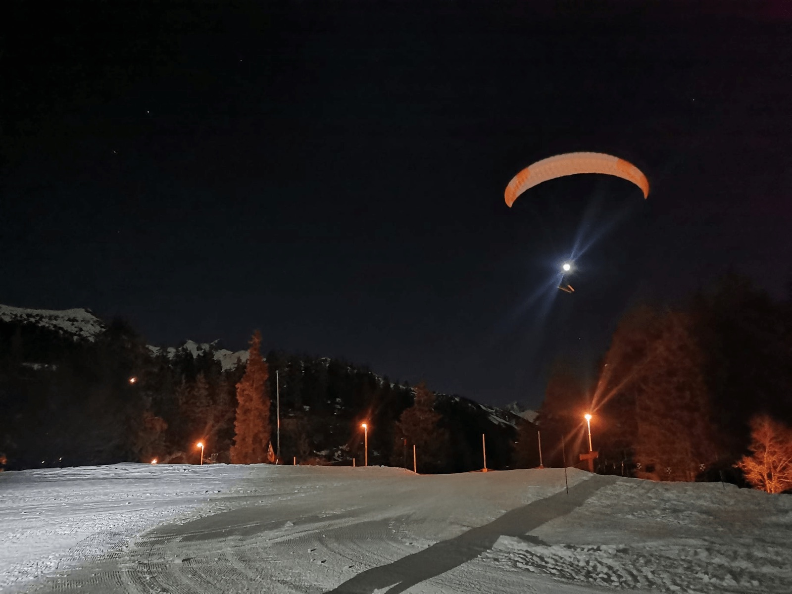 Parapente éclairé dans la nuit au-dessus d'une piste de ski enneigée